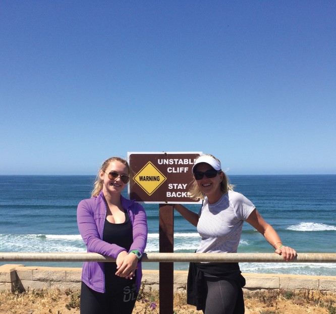 Mother and daughter pose on coastal cliff during workout hike