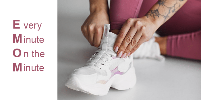 woman laces white tennis shoes with 'EMOM' written next to it