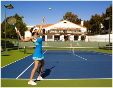 Woman in blue outfit serves tennis ball during PFC's tennis fitness camp