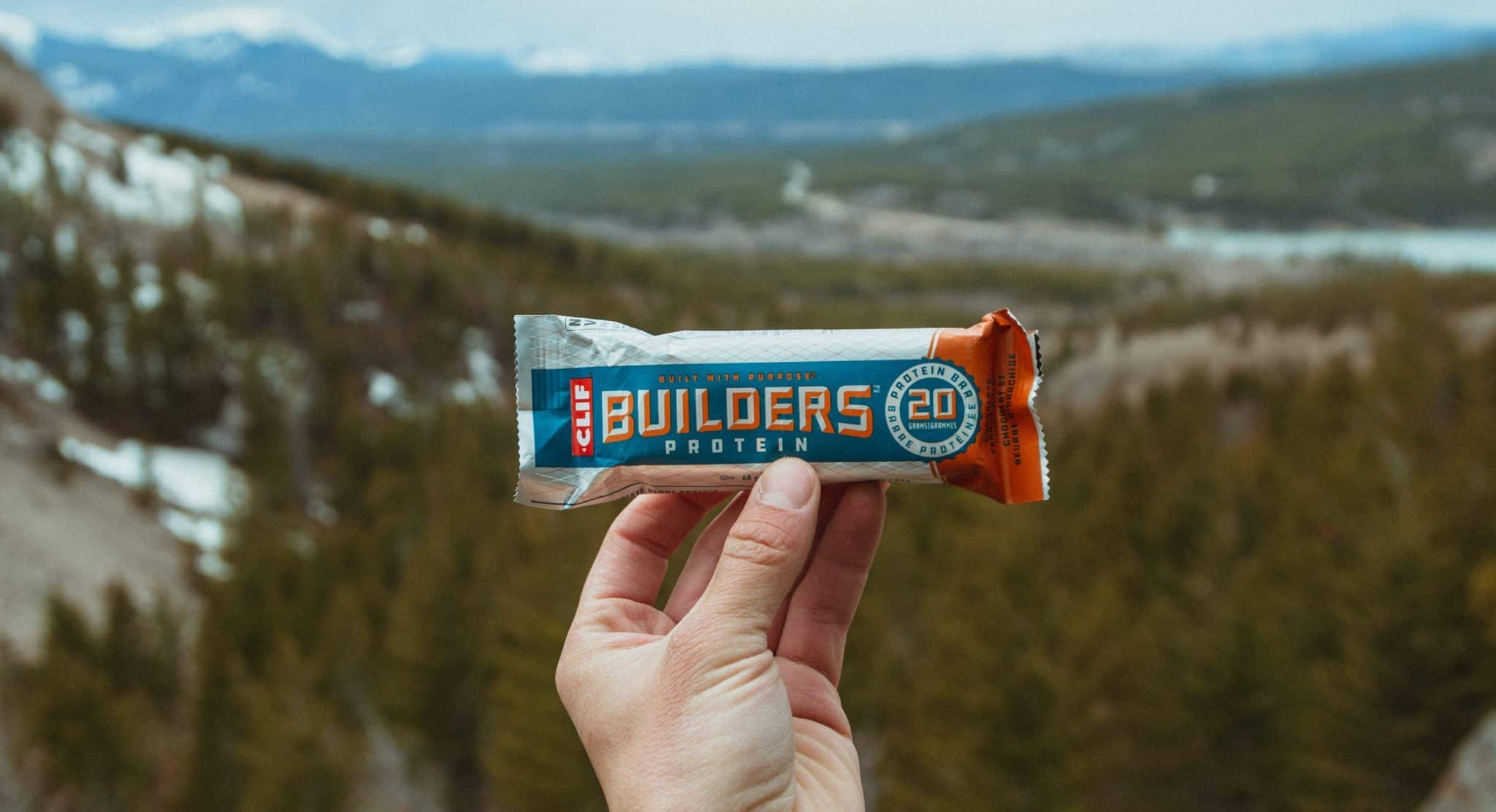 hand holding clif builders protein bars at the top of a mountain in winter