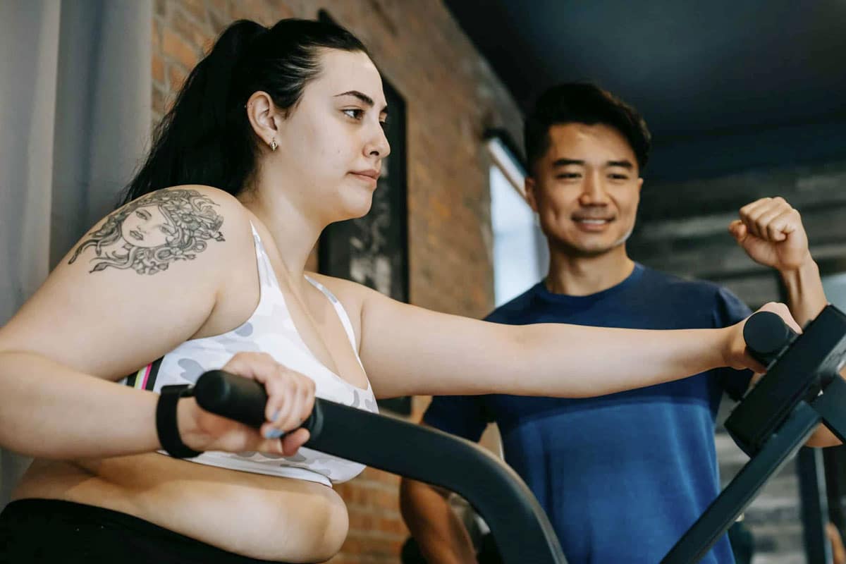Woman exercises on machines while trainer encourages her