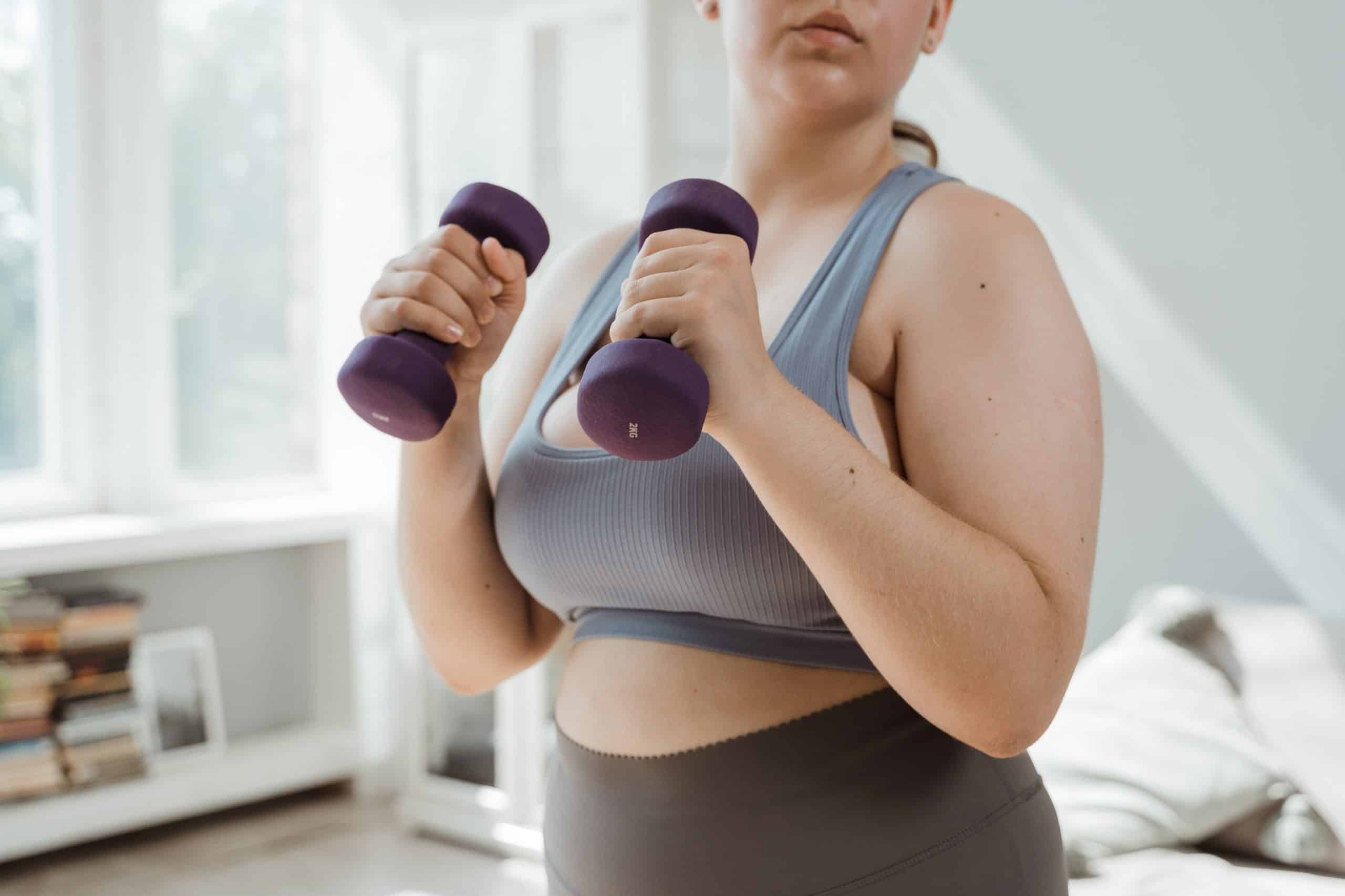 woman in athletic clothing holds dumbbells in home
