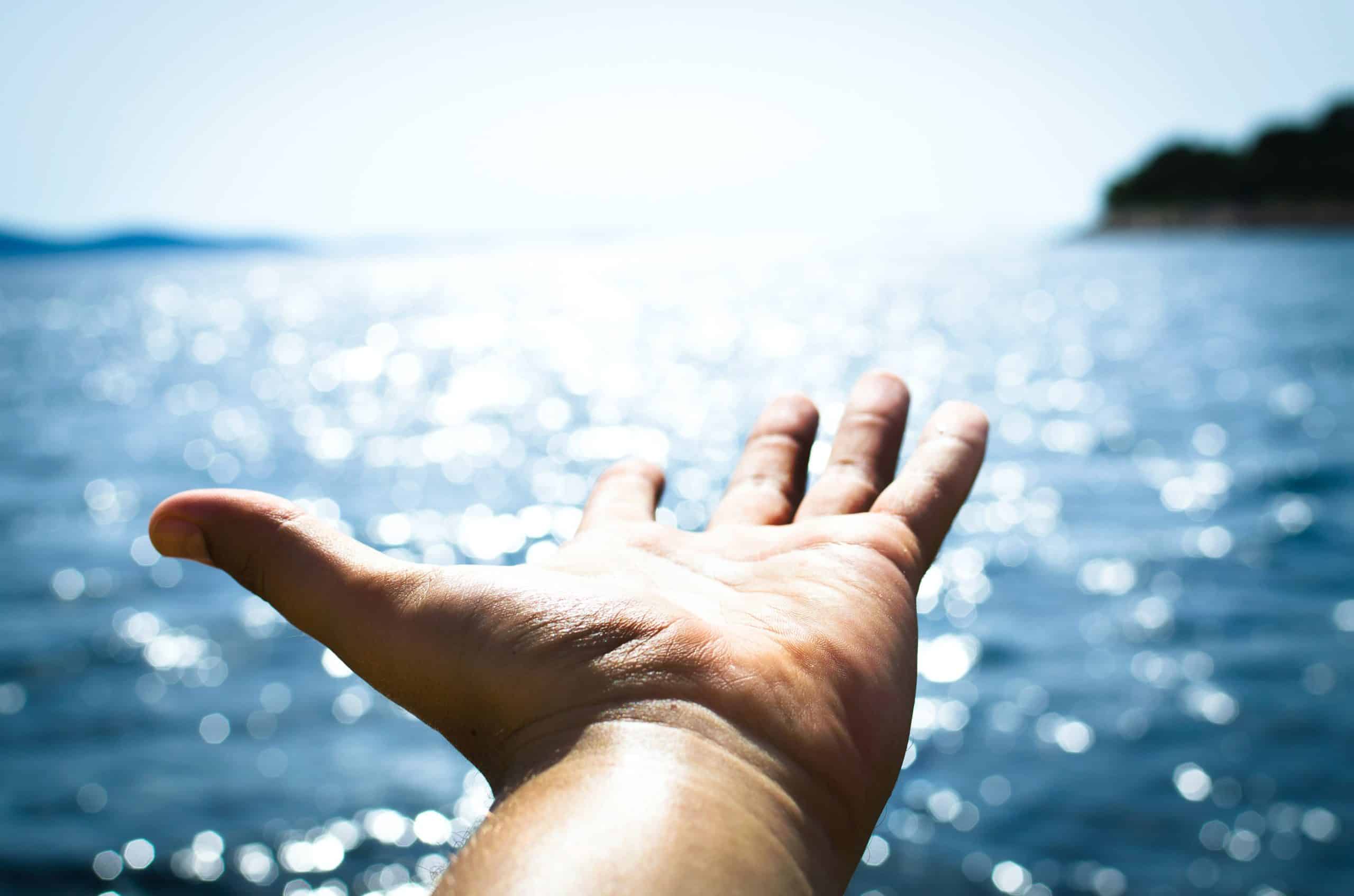 outstretched hand against ocean and cliff background