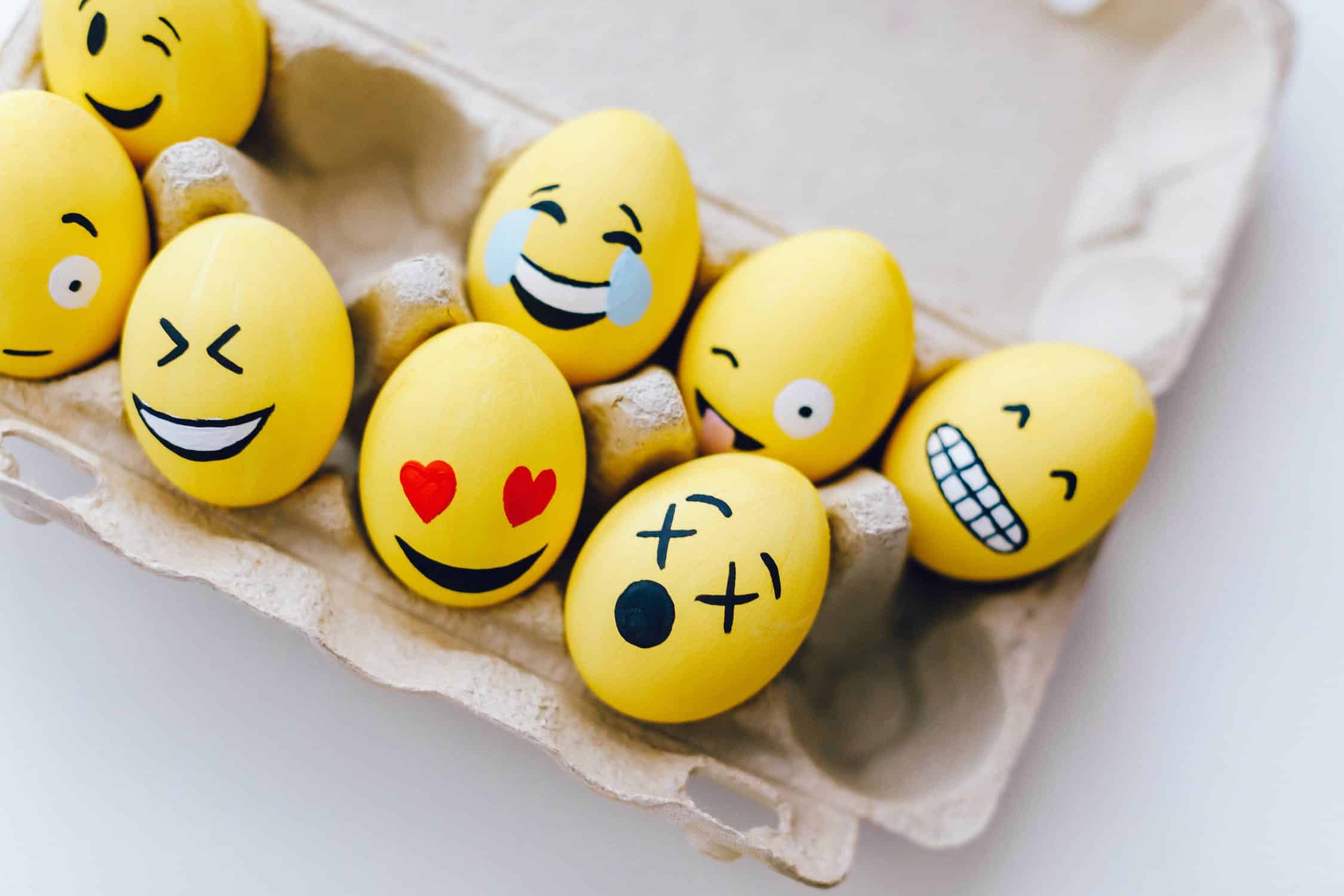 7 yellow eggs with emojis painted on them in carton