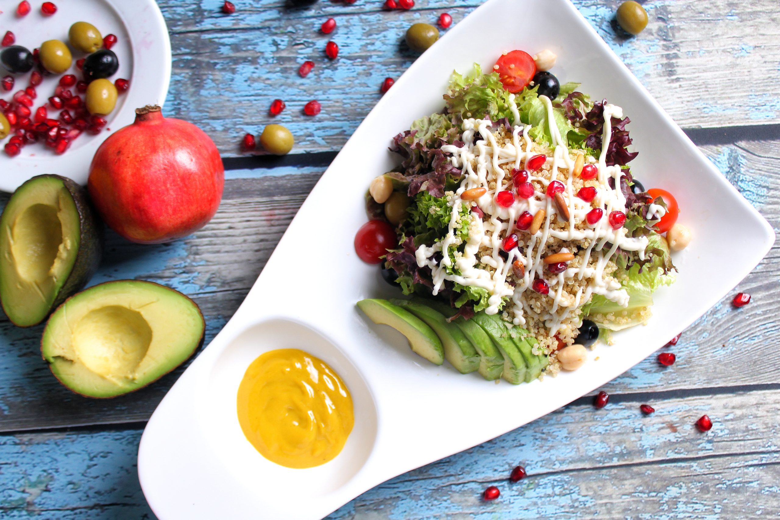 Plate with salad, veggies, dressing and pomegranates on a bright blue table