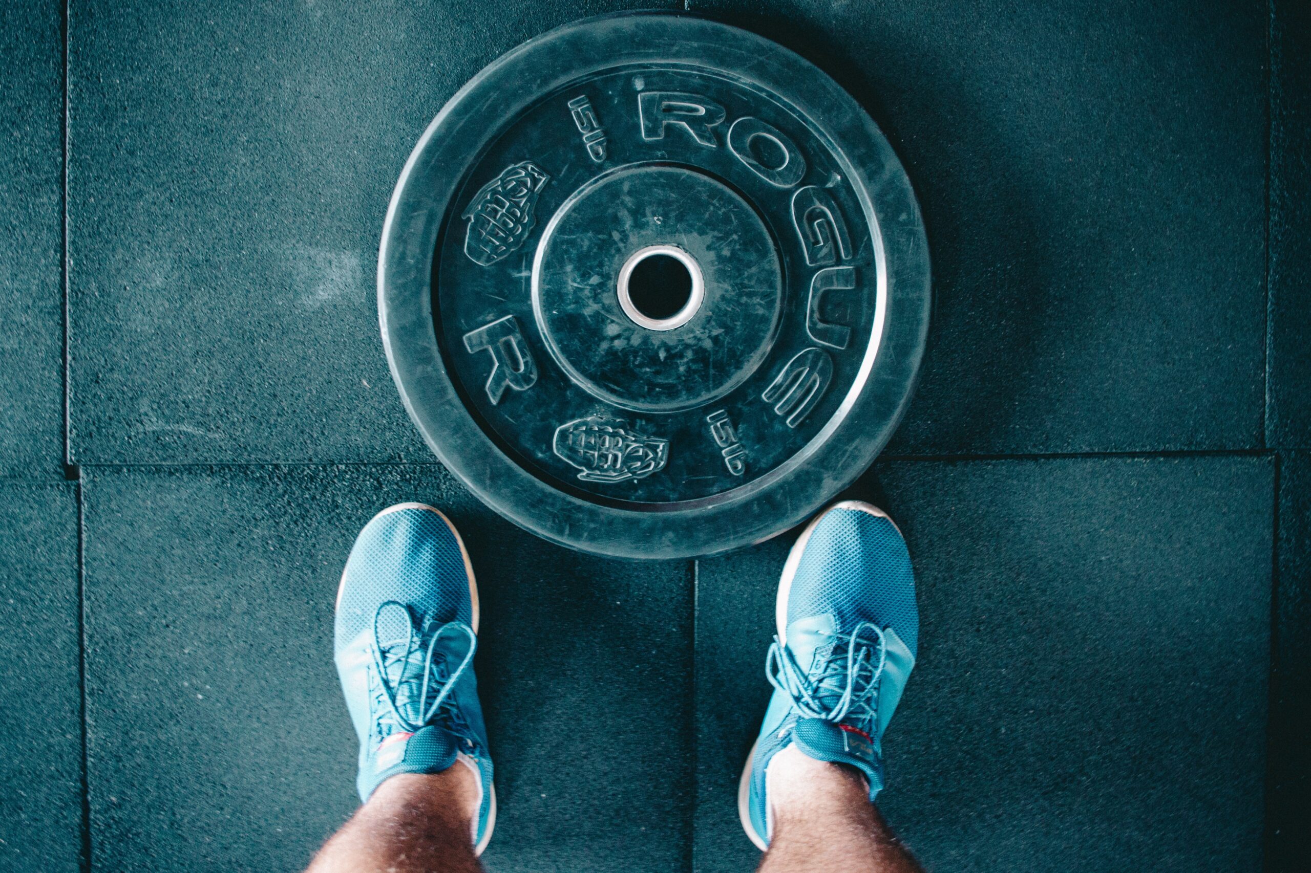 man's legs stand next to weight plate against a gym floor