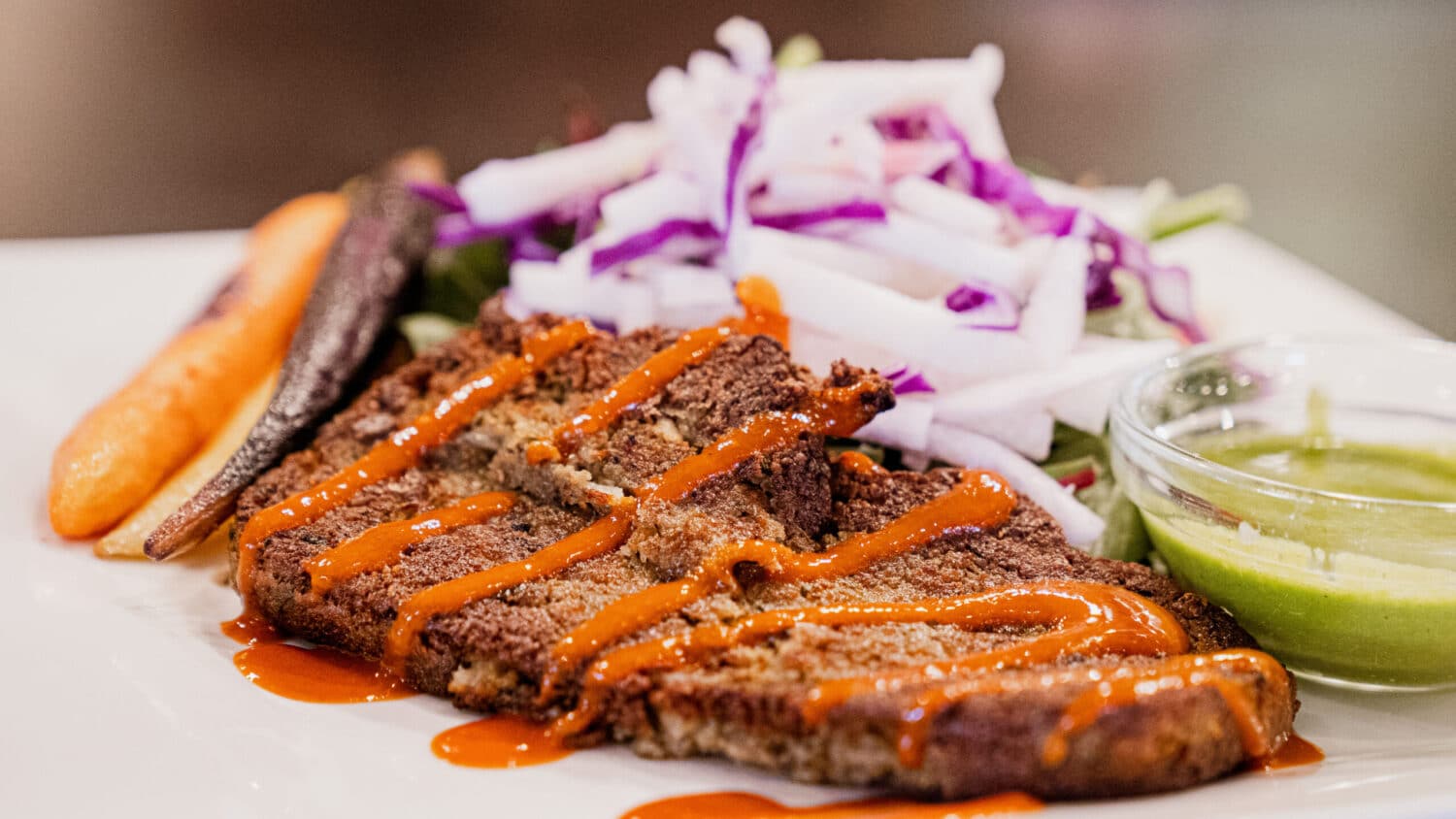 Lentil gyro meat on a plate with green sauce and heirloom carrots