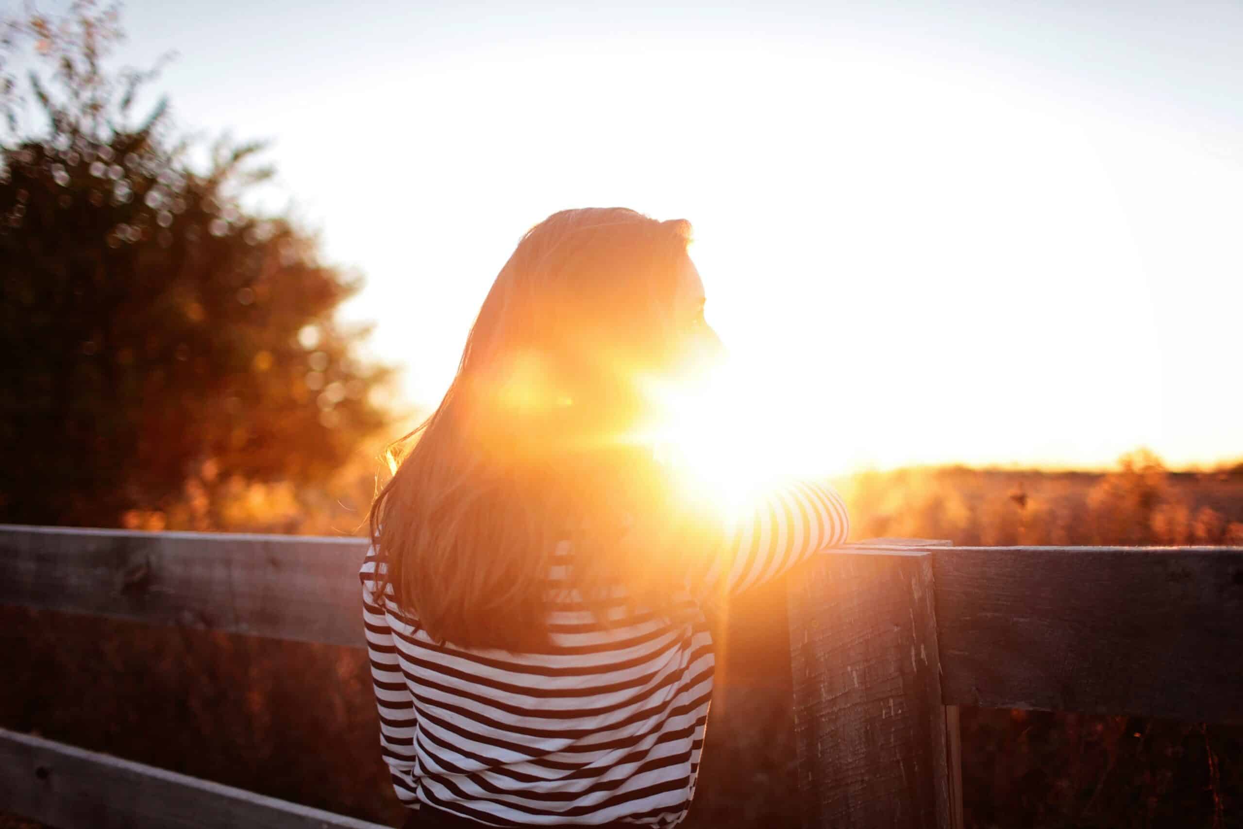 woman in striped shirt stands against fence at sunset