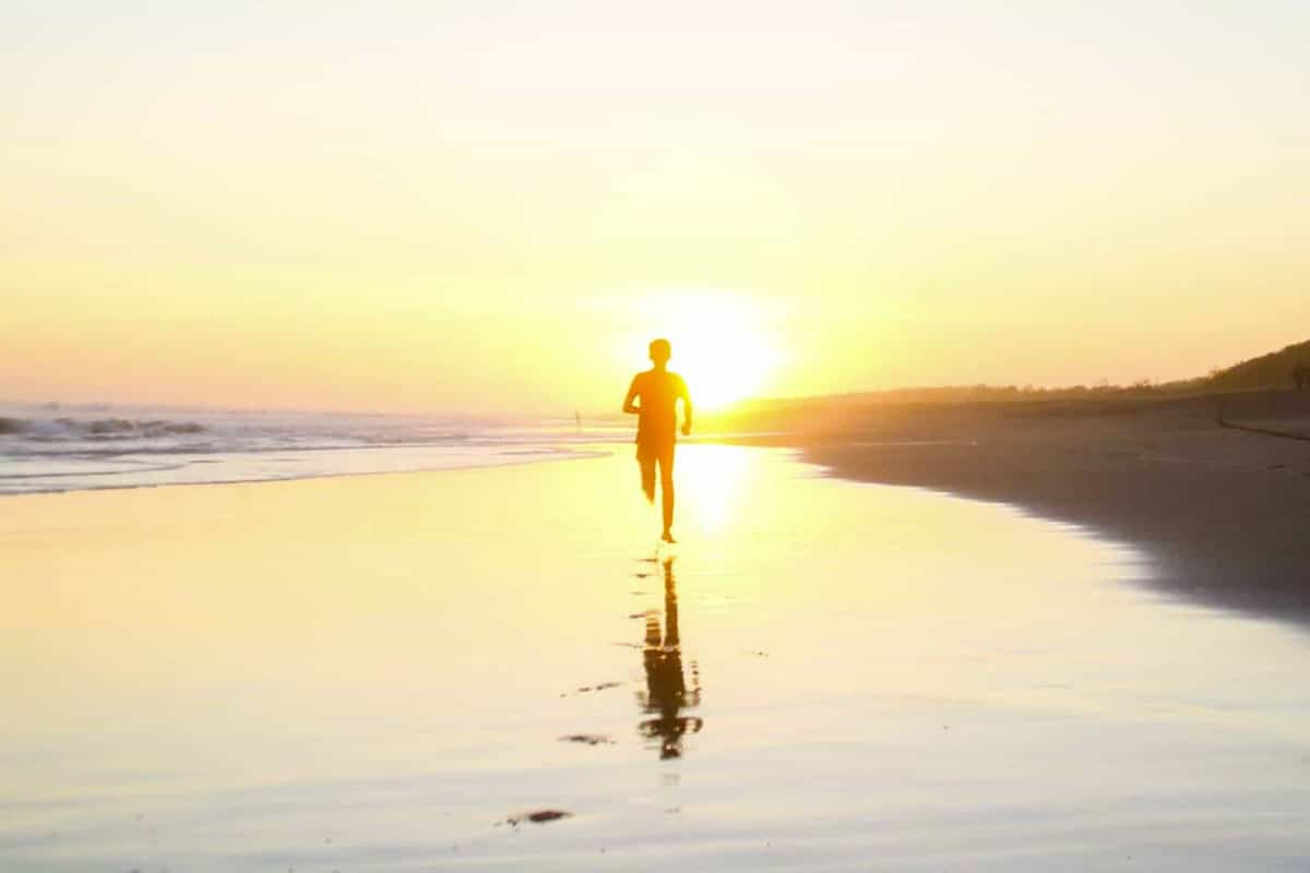 person runs along the beach at sunset