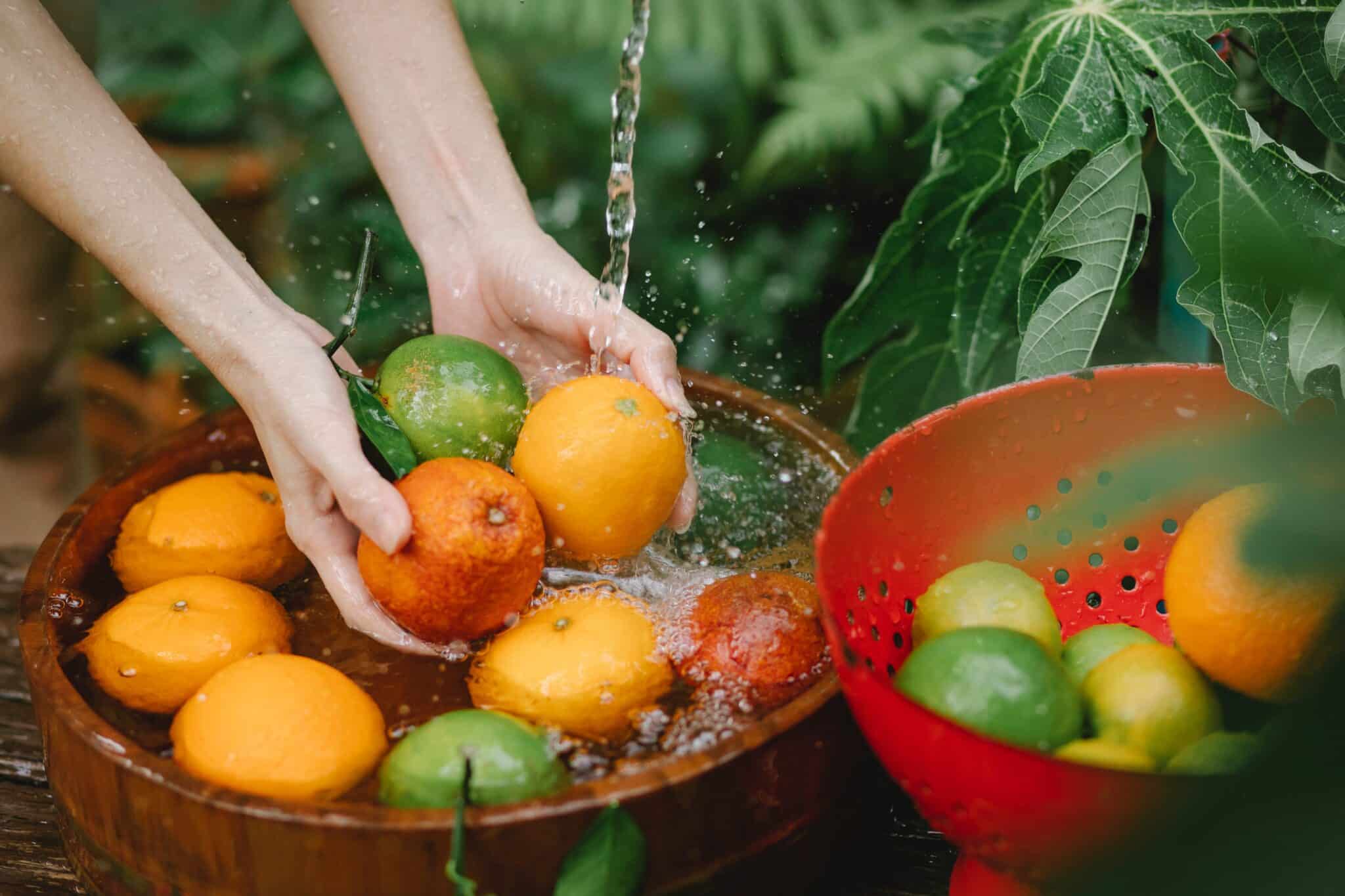 hands washing fruits near greenery