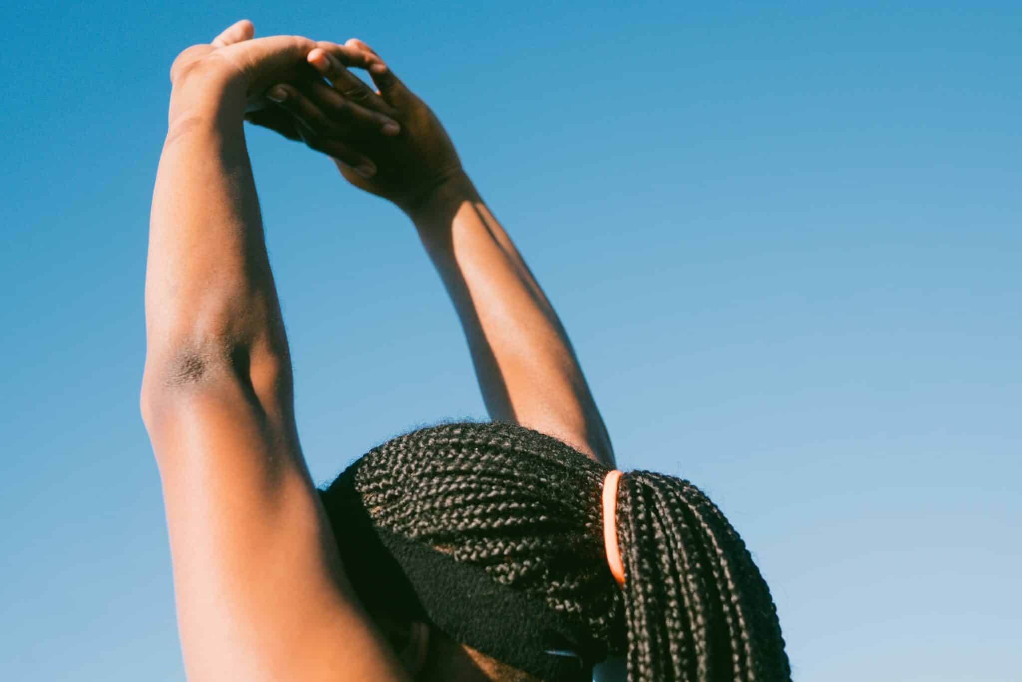 woman with hair in ponytail stretches her arms in the air