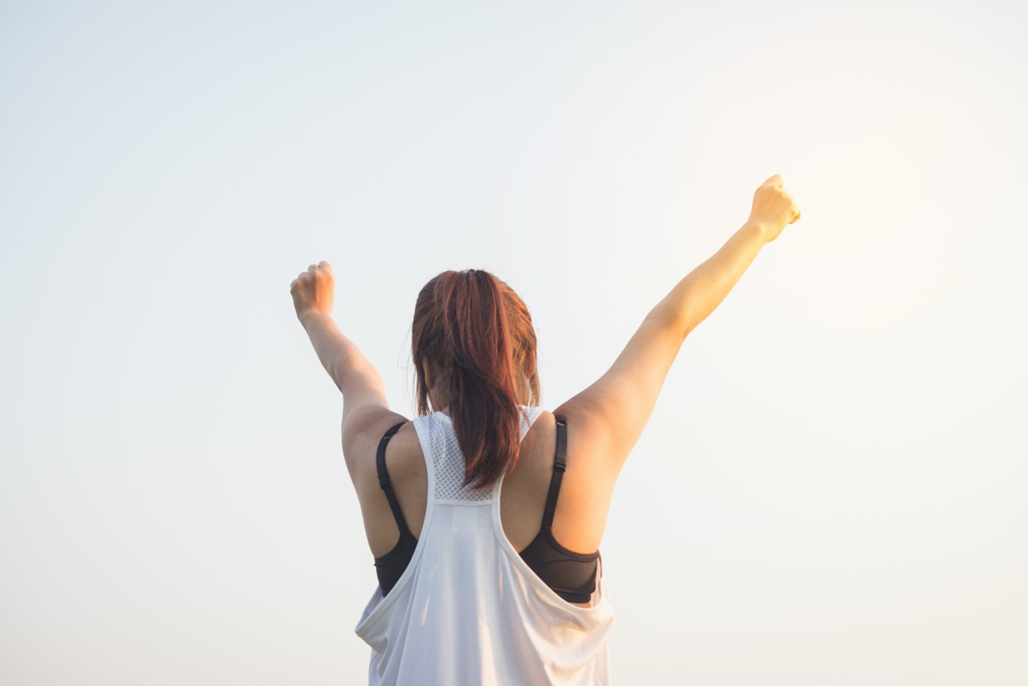 woman in tank top holds arms in the air