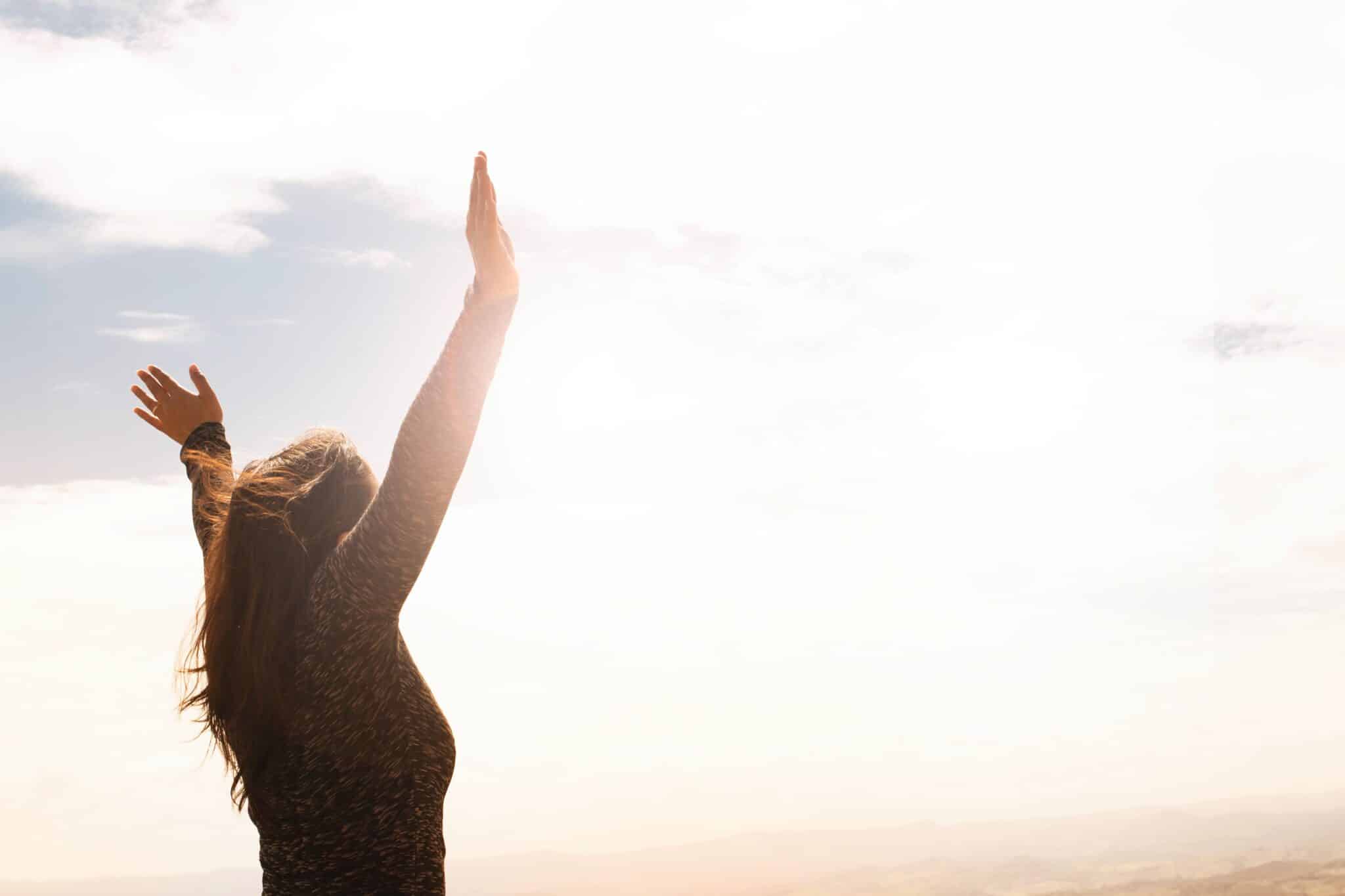 woman holds arms high in the air at sunrise