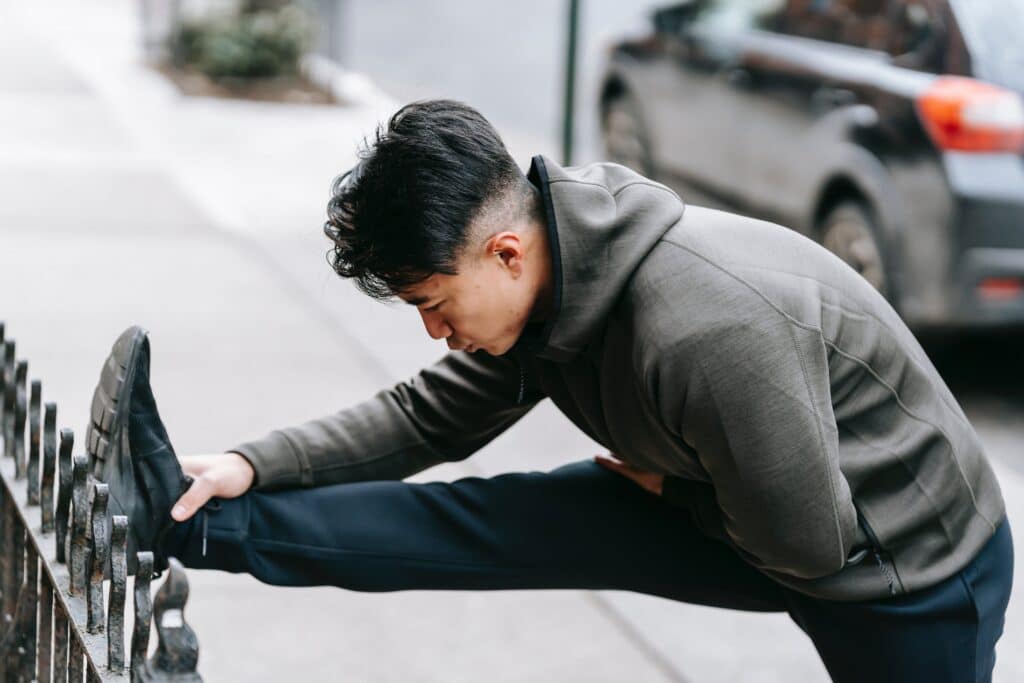 Man stretching and balance training on street as he prepares to run.